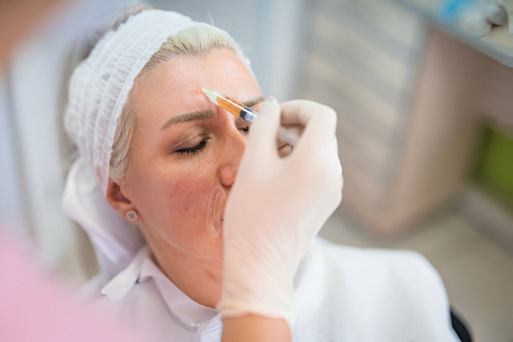 Woman receiving cosmetic injection in forehead.